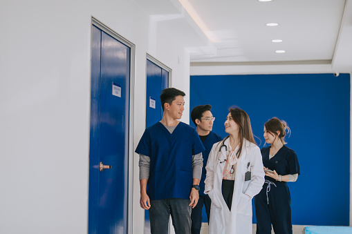 Asian Chinese Doctors and nurses discuss together on patient diagnosis treatment work during walk in the way in hospital near reception counter