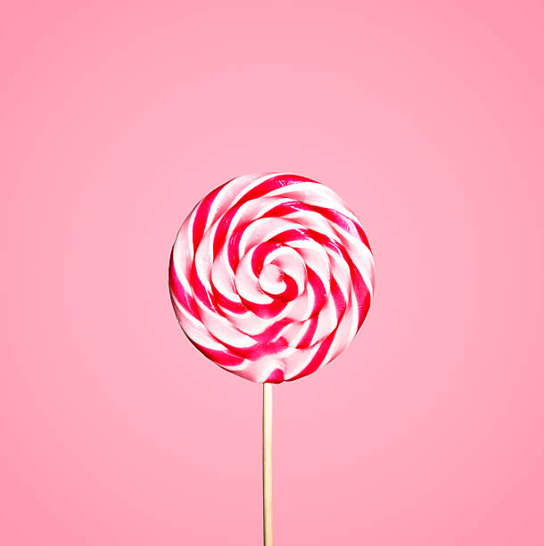 Colorful red and white lollipop candy on pastel pink background. Sweet sugar candy swirl in modern fashion style. Minimal flat lay design. Food fun for kids concept.