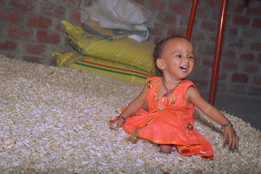 Cute baby girl having fun on a pile of garlic, rural home environment