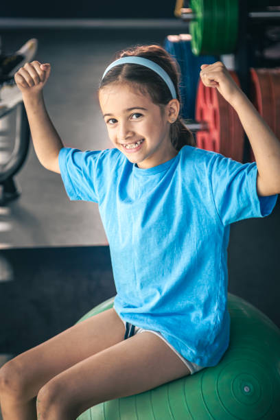 istock Charming little girl is shows her biceps, working out at gym. 1628976310