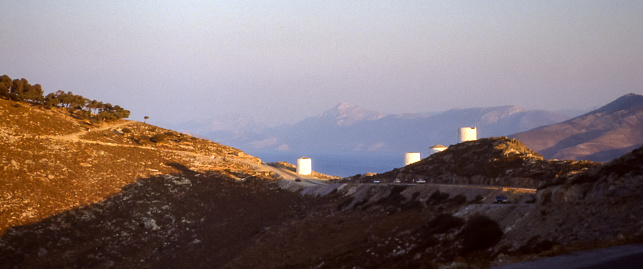 Leros Island, Greece - Aug 1990: white windmills lined up on a windswept mountain saddle on the island of Leros