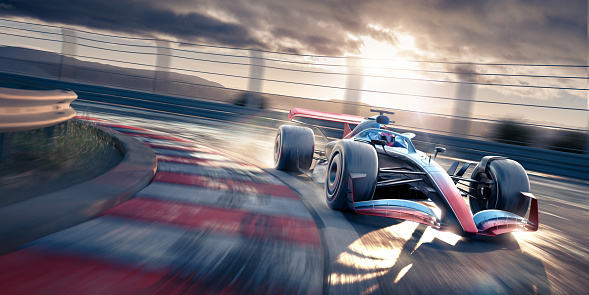 A generic blue and red racing car moving rapidly around a corner on a racetrack at dusk or dawn, under a cloudy sky. There is water spray coming from the tyres and motion blur on the track and background.