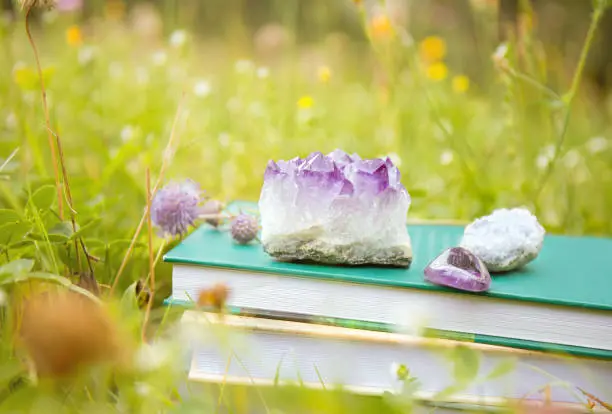 Self help or esoteric theme books in stack with crystal geodes outdoors in sunny summer day with blokeh nature meadow garden on background.