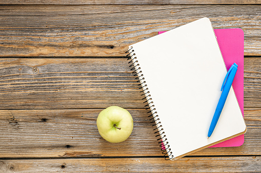 Notebooks and an apple on a wooden background, top view, the concept of school, office, copy space.