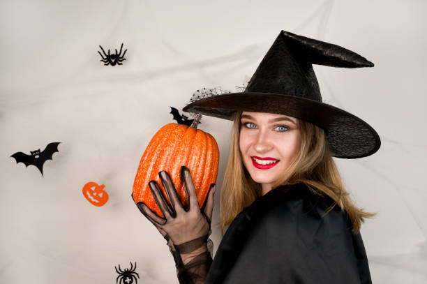 istock Young smiling blonde dressed as a witch holding pumpkin against halloween background. Copyspace 1628996448
