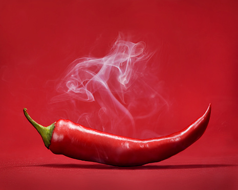 Red hot chili pepper on red background with smoke. Still life with steam mexican paprika spice.