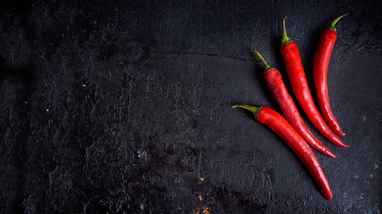 Red hot chili peppers on black rustic textured slate from above. Food background with spicy chilli paprika. Top view.