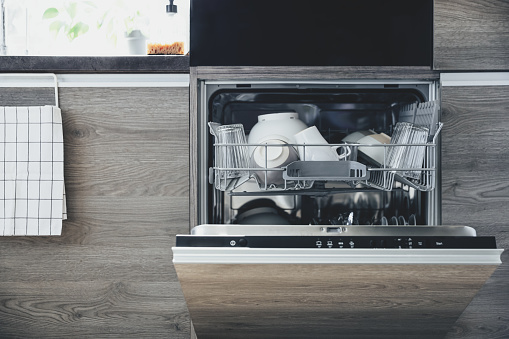 Closeup of opened automatic stainless built-in dishwasher machine inside modern home kitchen with clean utensil. Doing household chores, daily home routine, housework. Interior with kitchen appliances