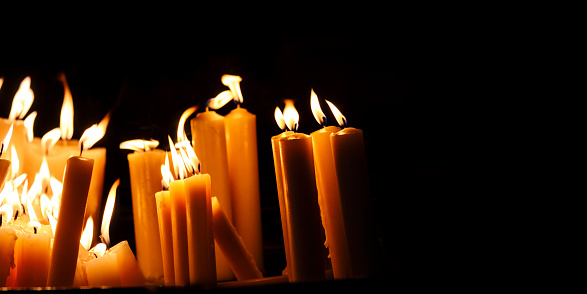 Religious candle light on black background. Yellow candlelight flame in dark christian church at night. Christian religion worship.