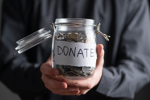 person holding a glass jar with metal coins, money donations concept