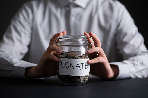 person holding a glass jar with metal coins, money donations concept