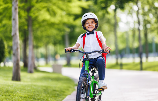 Happy african american child schoolboy in a helmet and with a briefcase rides a bike to school