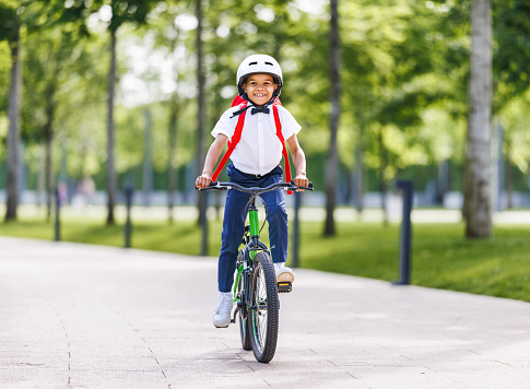 Happy african american child schoolboy in a helmet and with a briefcase rides a bike to school