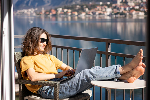 Young happy woman using laptop while sitting on the balcony on a summer day