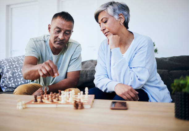 istock Senior couple, chess match and home with thinking, strategy and mindset for brain power, relax and bonding. Elderly woman, man and sofa with board game, ideas and brainstorming for challenge in house 1629078944