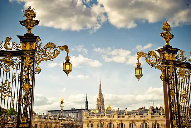 Detail of Stanislas square in Nancy (Lorraine, France) : golden iron gates and lamps typical of rococo style in the 18th century. St Epvre church in the background.