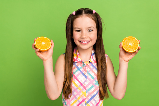 Photo of lovely cheerful schoolgirl toothy smile hands hold two orange fruit halves isolated on green color background.