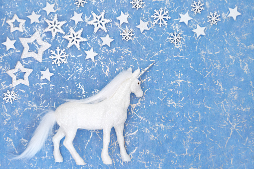 Christmas unicorn magical ornament with snowflake and star decorations on mottled blue background. Festive fantasy happy holidays design for Yule, Noel, New Year season.