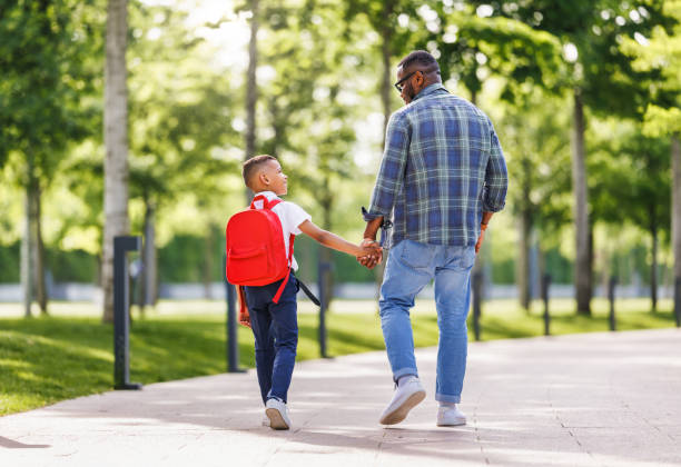 istock Schoolboy looking at father with smile while going with dad to first grade in school on sunny autumn day 1629097061