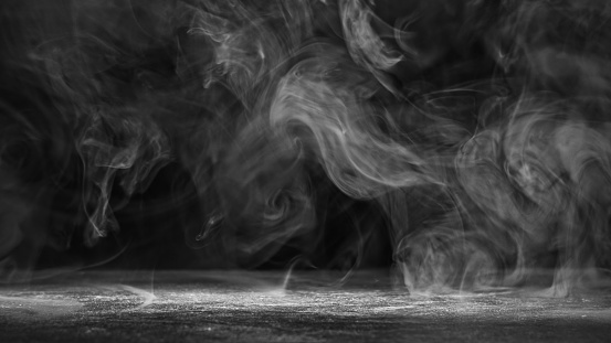 A flame of a burning white wax candle with smoke emanating and rising on a black background