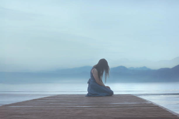 바다의 부두에 무릎을 꿇고 외로운 여자는 푸른 분위기에서 감정에 휩싸입니다 - ��무릎 꿇기 뉴스 사진 이미지