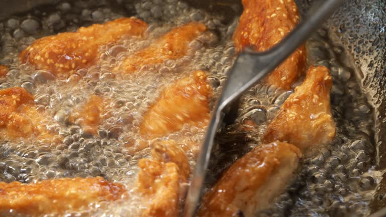 using a spatula to turn chicken wings in boiling oil on a hot pan.