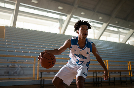 Male basketball player dribbling basketball while looking away during practice on court.
