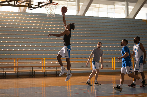 Male basketball player throwing basketball towards hoop to score during practice on court.