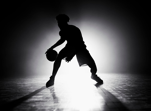 Silhouette of male basketball player dribbling basketball while playing on sports court during practice.