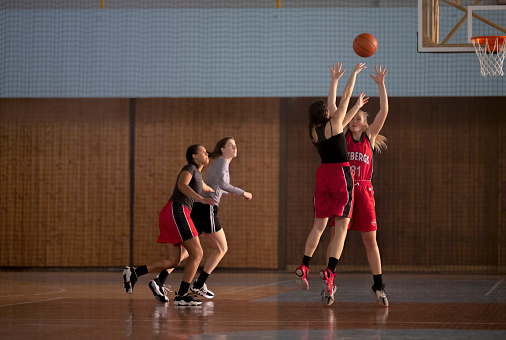 Female basketball player throwing basketball towards hoop to score during practice on court.