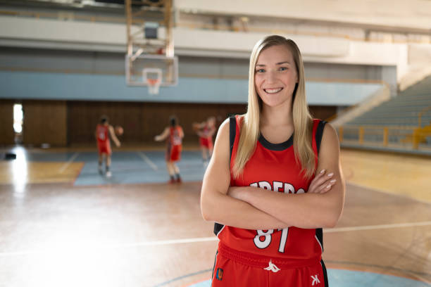 Portrait of smiling young woman with arms crossed standing on basketball court during practise.