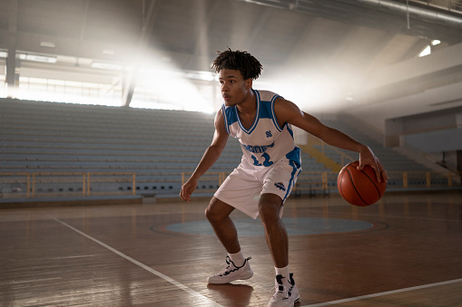 Male basketball player dribbling while playing basketball during practice on court.