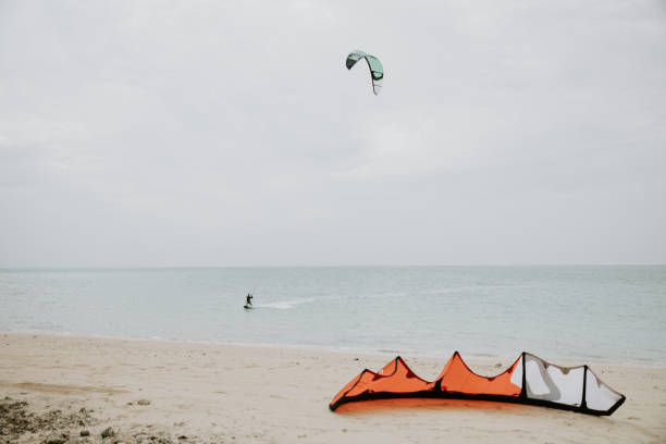 A wide-angle shot captures the serenity and excitement of kite surfing, as a skilled surfer rides the waves, framed by the vastness of the open sea.