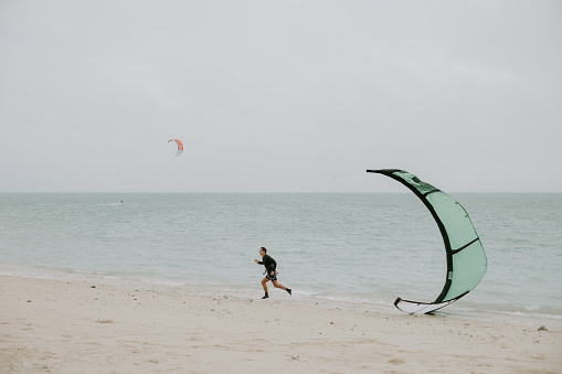 A kite surfer running around the beach with his kite, checking if the equipment is ready for a training session.