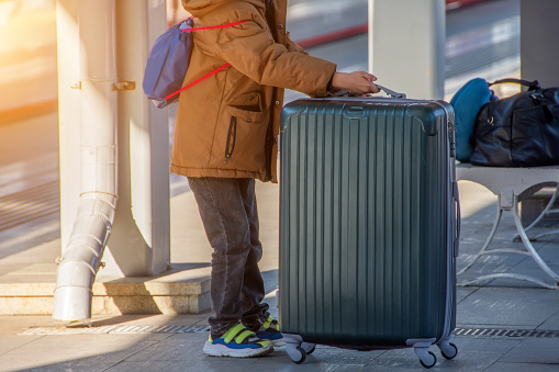 The child holds a large suitcase on wheels on the railway platform