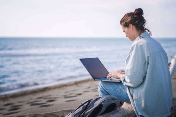 istock Young caucasian woman freelancer working on a laptop while sitting on a sandy beach. 1629167319