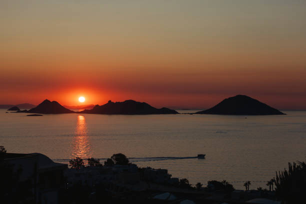 Turkish Aegean view at Turgutreis during sunset, with a motorboat sailing across the scene between distant islands and the coastline.