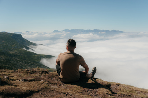 A young man sitting on top of a mountain with a sea of clouds below him