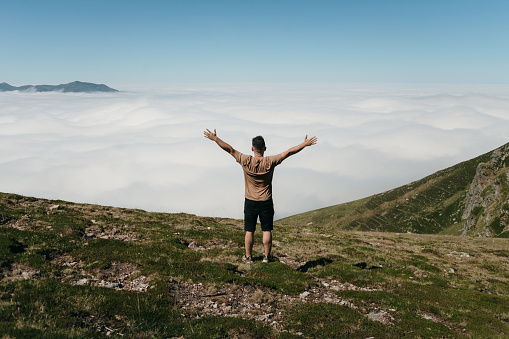 Rear view of a man with arms raised standing in a mountain area facing a sea of clouds below