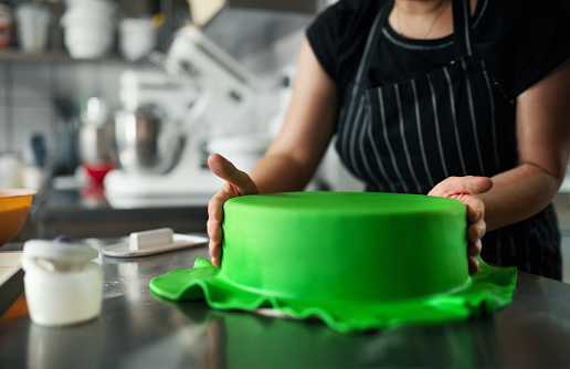 Closeup of unrecognizable women covering a cake with a green colored fondant.