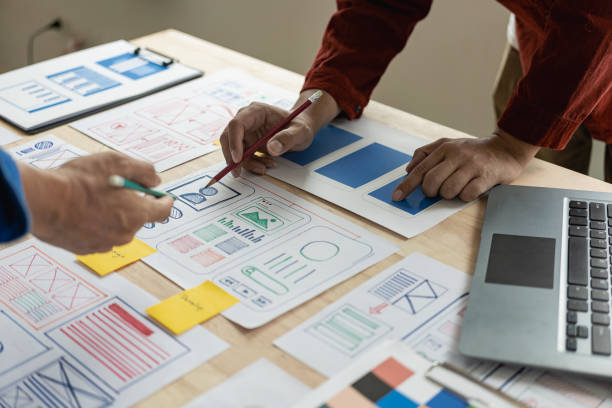 istock A team of web designers are working together to develop a mobile responsive website with UI/UX front end design concepts. A team of UxUi developers are working together at a wooden workbench. 1629201767