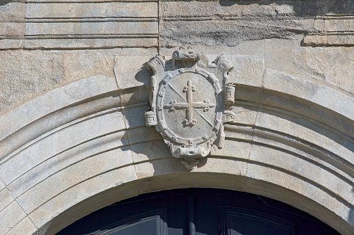 Part of the facade. Medieval Catholic church of Sao Goncalo in Amarante, Portugal. Coat of arms with a cross