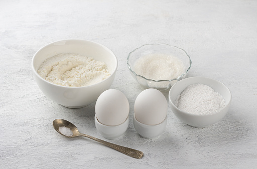 Baking ingredients: flour, sugar, powdered sugar, eggs, salt on a light gray background. Cooking delicious homemade cookies.