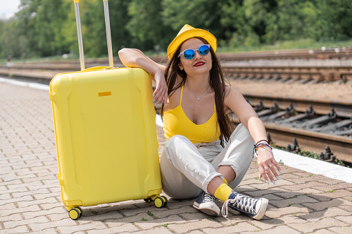 Incendiary journey: a young tourist in a bright style of clothing and with a suitcase set up for adventure. Free spirit of adventure: a girl in yellow is ready to explore new places. High quality photo