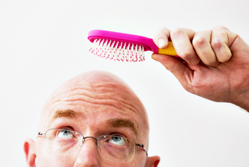 In an ironic image, a bald man looks up, eyebrows raised, as he attempts to brush his non-existent hair with a girl's pink hairbrush.