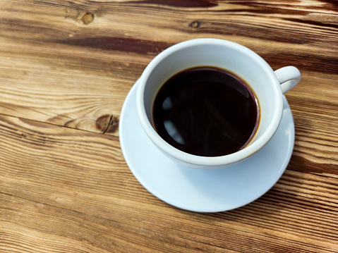 Cup of black coffee without milk in round white cup on brown wooden table background
