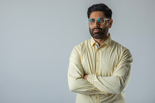 Portrait of confident mid adult businessman wearing eyeglasses with arms crossed standing against white background
