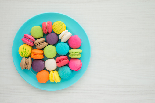 Colorful France macaroons on blue plate and white table background copy space. French food, culture, food design concept.