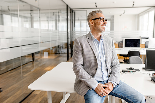 Close-up of mid adult male marketing freelancer with arms crossed, wearing casual clothing, and looking at camera with contented expression in coworking office.