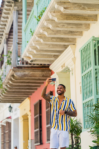 Latin man from Cartagena Colombia between 20 and 29 years old, enjoys being single while vacationing alone in beautiful Cartagena wandering through its colonial streets and enjoying a hot day and taking photos with his cell phone